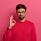 No problem concept. Bearded man makes okay gesture, has everything under control, all fine gesture, wears spectacles and jumper, poses against pink background, says I got this, guarantees something No problem concept. Bearded man makes okay gesture, has everything under control, all fine gesture, wears spectacles and jumper, poses against pink background, says I got this, guarantees something