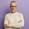 Headshot of confident mature European male pensioner keeps arms folded, wears optical glasses and white sweater, being sure in something, isolated over purple background. People and aging concept Headshot of confident mature European male pensioner keeps arms folded, wears optical glasses and white sweater, being sure in something, isolated over purple background. People and aging concept